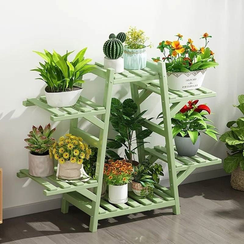 Green plant stand with various potted plants against a white wall.