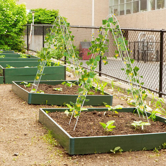 Row of green raised garden beds with plants in an urban setting.
