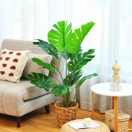 Living room with a large green plant in a woven basket, beige sofa with patterned cushions, and a small round table.