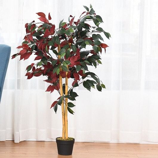 Artificial potted plant with red and green leaves on a wooden floor with white curtains in the background.