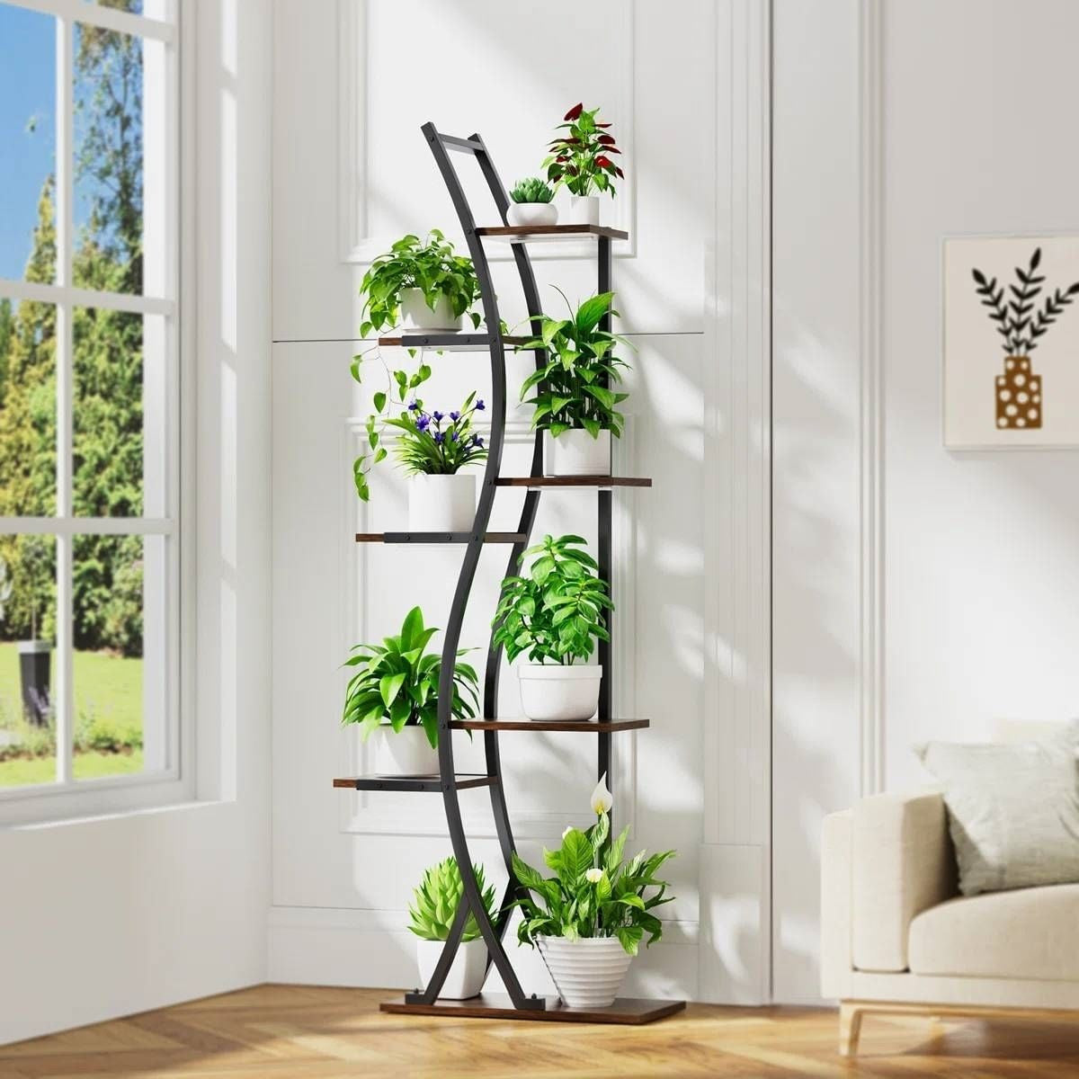 Tall black metal plant stand with multiple shelves holding potted plants in a bright room.