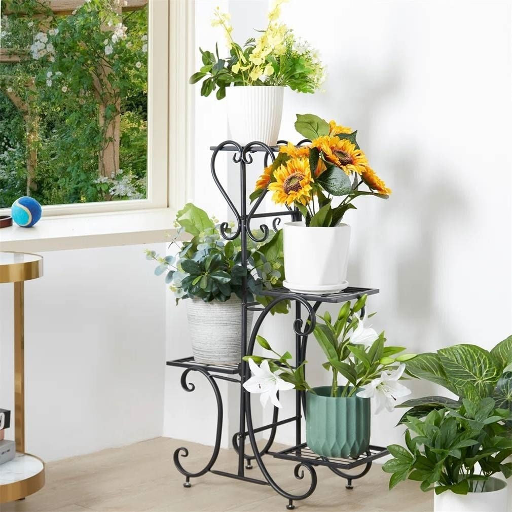 Black metal plant stand with various potted plants in a room with a window.