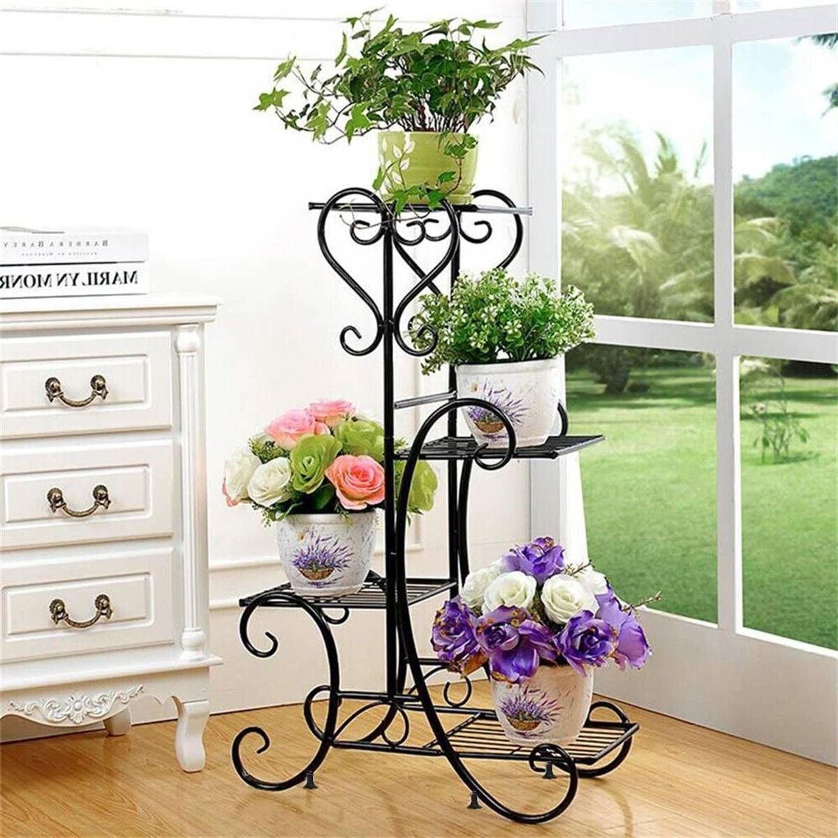 Black metal plant stand with flowers and plants in a room with a window view.