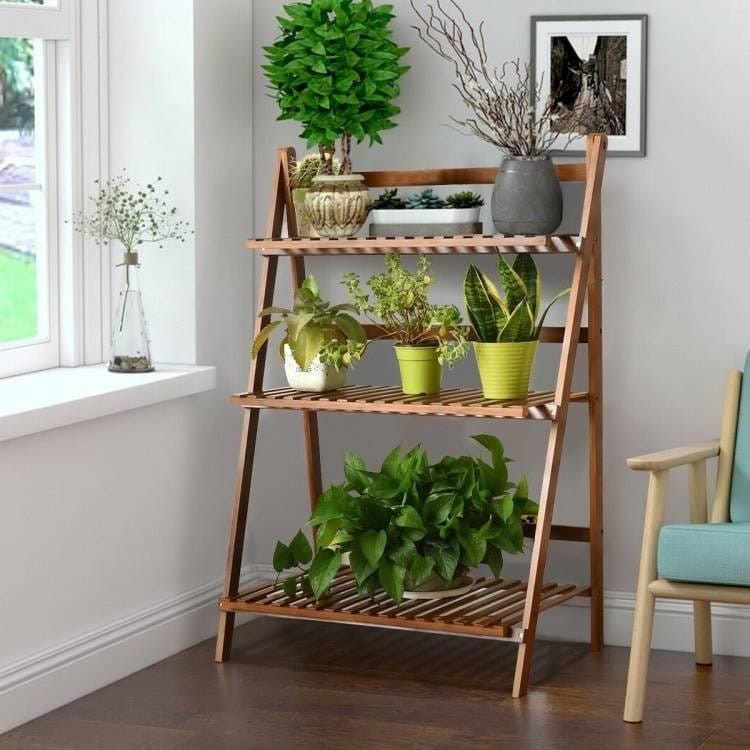 Wooden plant stand with various potted plants in a room with a window and chair.