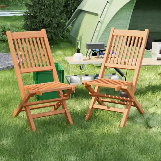 Two wooden chairs on grass with a camping setup including a tent and cooler.