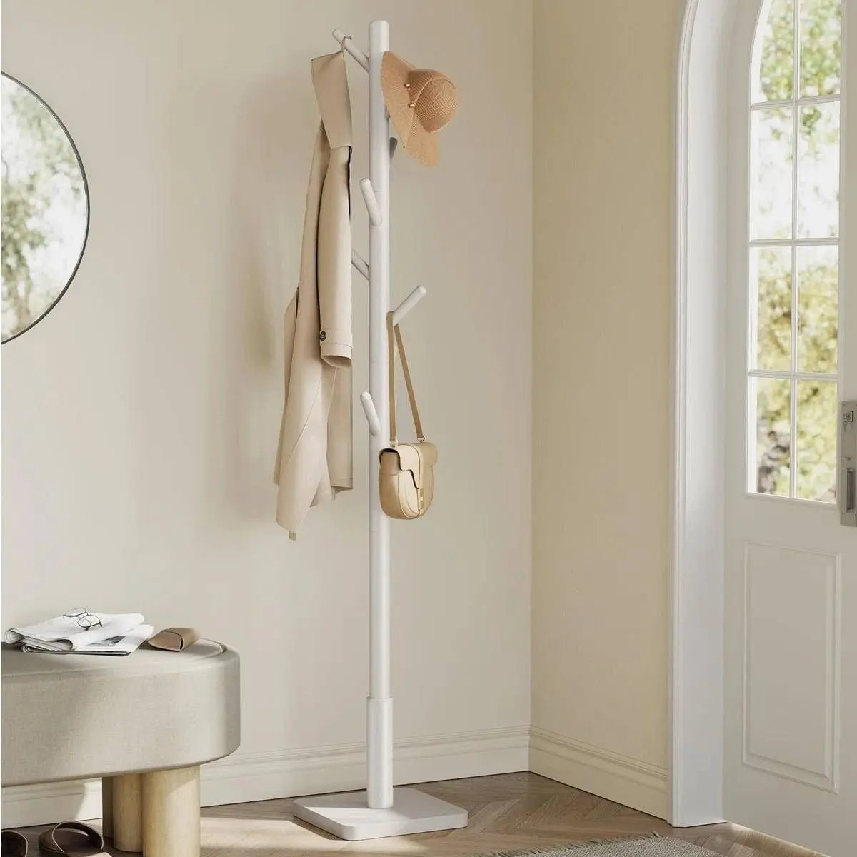 White coat stand with a beige coat, hat, and handbag against a neutral wall.