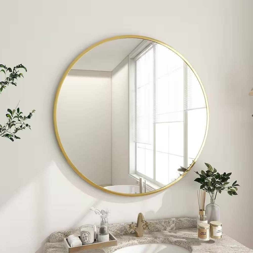 Round gold-framed mirror on a wall above a countertop with decorative items.