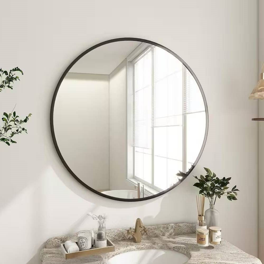Round mirror on a wall above a bathroom counter with various items.