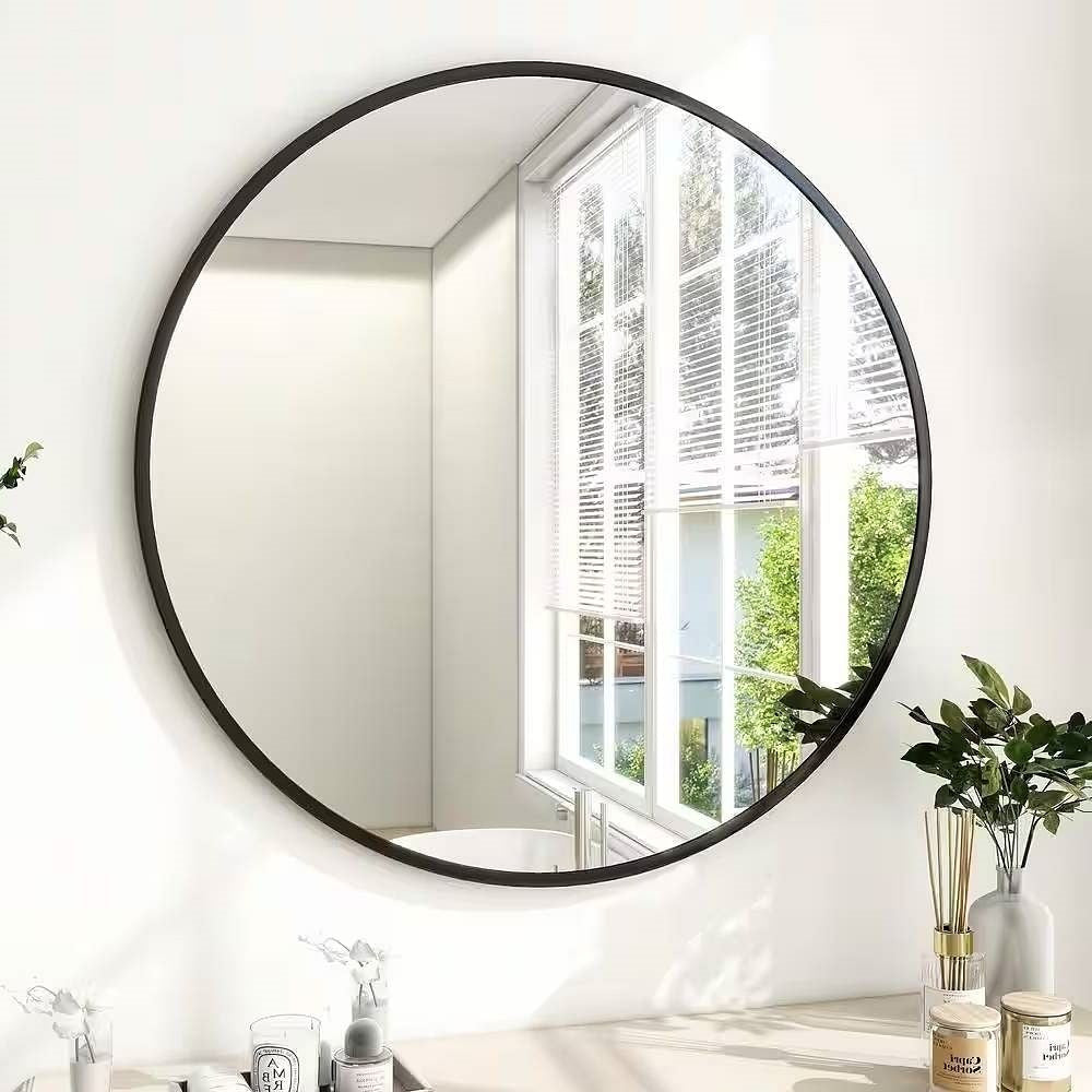 Round wall mirror with black frame in a room with a window and plants.