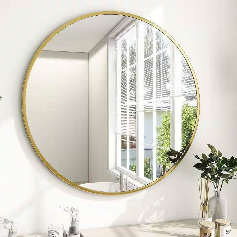 Round gold-framed mirror on a white wall with a window in the background