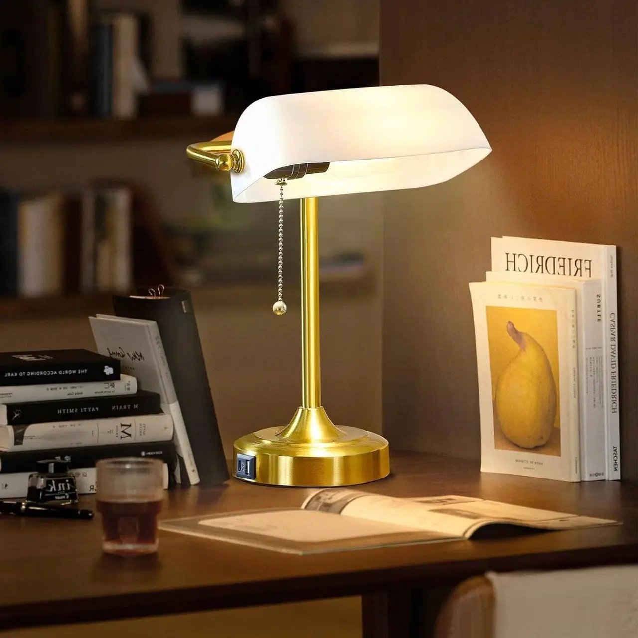 Gold desk lamp on a wooden surface with books and a glass of tea in the background